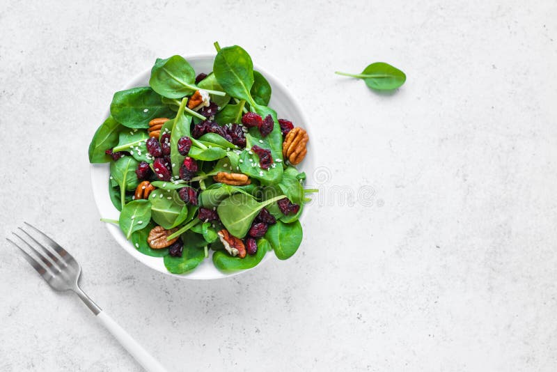Spinach salad with pecan nuts and dry cranberries on white background, copy space. Heathy clean vegan raw food, fresh salad. Spinach salad with pecan nuts and dry cranberries on white background, copy space. Heathy clean vegan raw food, fresh salad